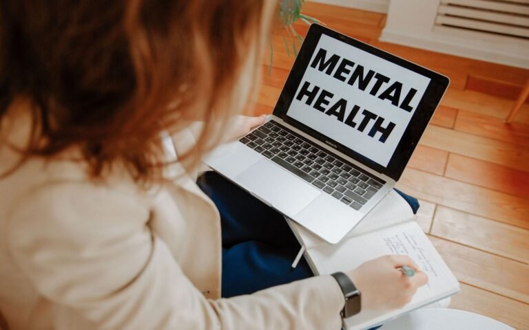 Person at home taking notes during a telehealth mental health visit on a laptop